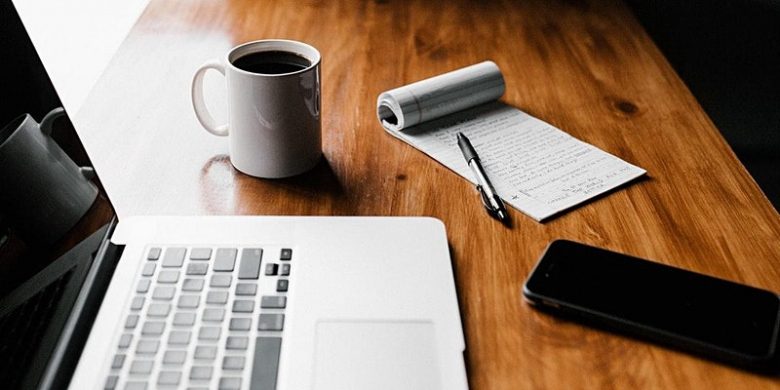 Photo of a desk with a laptop, coffee, and notepad